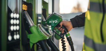 editorial picture of a mans hand on a green fuel pump that says HVO100 and is putting it inside of a regular diesel fuel pump at a modern gas station in europe, another person is making notes for auditing purposes and wearing a safetvest --ar 16:9 Job ID: c9eb3abc-f677-4436-b320-d51dab3f23fc